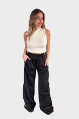 Pantalón negro de tela deportiva con cintura elástica ancha y cordón ajustable. Presenta corte amplio, bolsillos laterales y una franja blanca vertical a lo largo de cada pierna.