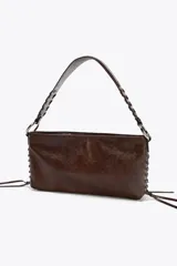 Bolso de hombro marrón de cuero sintético con dos bolsillos frontales con cremallera y tiras decorativas. El asa es trenzada y tiene herrajes metálicos.