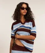 Remera oversized de punto con rayas horizontales en tonos marrón, celeste y blanco. Presenta cuello polo y mangas cortas.