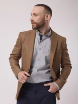 Saco de lino color tostado, de corte clásico, con solapa de muesca, cierre de dos botones, bolsillo en el pecho y bolsillos laterales con solapa.