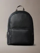 Mochila de piel sintética granulada color negro, con asa superior de tela gris y correas ajustables. Presenta un bolsillo frontal con cierre y el monograma de Calvin Klein en relieve en la parte inferior.