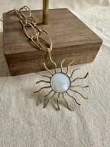 Collar dorado con cadena de eslabones grandes y dije de sol con centro de nácar.