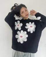 Sweater tejido negro con cuello redondo y tres flores blancas bordadas en el frente.
