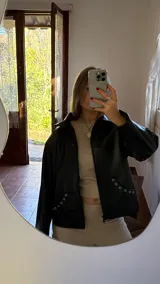Campera negra de ecocuero con cierre frontal y bolsillos laterales con detalle de ojales metálicos.