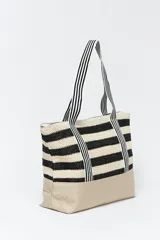 Bolso de playa de paja con rayas horizontales negras y beige. Asas de tela con rayas verticales blancas y negras.