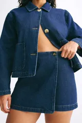Short pollera cruzado de tiro alto en sarga de algodón color azul denim con botón a un lado, cierre oculto adelante y bolsillos insertados decorativos atrás.