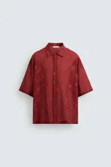 Camisa color ladrillo con estampado de flores en relieve, corte relaxed fit, cuello bowling, manga corta, bajo con aberturas laterales y cierre frontal con botones.