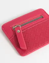 Tarjetero color fucsia de cuerina con diseño trenzado en la parte inferior y cierre superior con tirador.