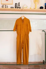 Mono color ocre de gabardina 100% algodón, con corte clásico, cierre frontal completo, pantalón largo con bolsillos, manga corta y cintura fruncida en la espalda.