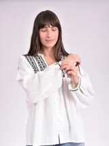 Camisa blanca de manga larga con bordado negro en el cuello y puños, con botones frontales.