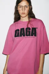 Camiseta rosa de algodón con efecto lavado, cuello redondo y manga corta. Estampado frontal con el texto "GAGA" en color negro.