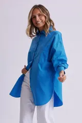 Camisa celeste de manga larga, corte oversize, con cuello clásico, cierre frontal con botones, bolsillo en el pecho y bajo redondeado.