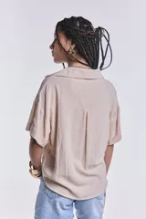 Camisa color beige de corte cropped, con cuello clásico, cierre frontal con botones y dos bolsillos de parche en el pecho.