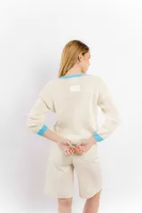 Sweater tejido de lana merino color crudo, con cuello, puños y ruedo acanalados en color celeste. Presenta un corazón celeste tejido en el frente.