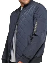 Campera bomber azul marino con diseño acolchado en forma de rombos, cierre frontal con cremallera, cuello, puños y dobladillo acanalados, bolsillos laterales y bolsillo en la manga con cremallera. Logotipo de Calvin Klein en la manga.
