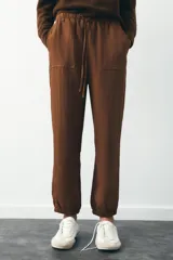 Pantalón jogger color gris claro, de tiro alto con cintura elástica ajustable con cordones, bolsillos delanteros y traseros con solapa, y puños elásticos en el bajo.