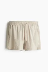 Short de baño color beige con textura de sirsaca, cintura elástica con cordón ajustable, bolsillos laterales y trasero ribeteado, aberturas laterales cortas y suspensor interior de malla.