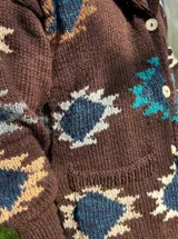 Saco de lana marrón con cuello esmoquin, cierre con botones y bolsillos delanteros. Diseño con motivos geométricos en tonos azul, beige y blanco.