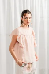 Blusa color rosa pálido de lino con volados en las mangas, corte ancho, cuello redondo y detalle de calado en el canesú.