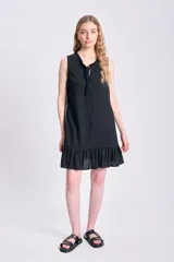 Vestido corto negro sin mangas, confeccionado en lino, con escote redondo con lazo y volados en el ruedo.