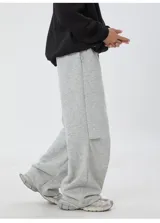 Pantalón deportivo gris jaspeado, corte ancho y holgado, con cordón ajustable en la cintura y detalle de etiqueta con texto en el bolsillo lateral.