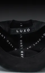 Gorra negra de gabardina con bordado rojo de la palabra "Ravers" en letra cursiva. Tiene cinta trasera de velcro para regular el ajuste.