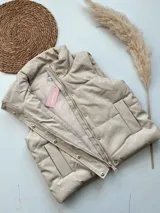 Chaleco de ecocuero color crudo, con diseño puffer y bolsillos, ajustable a los lados.