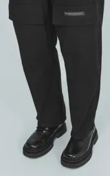 Pantalón cargo negro de corte recto con bolsillos laterales con solapa y etiqueta con texto en la pierna derecha.