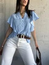 Camisa celeste con cuello mao, mangas cortas con volados y detalle de pinzas verticales en el frente.