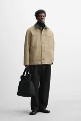 Parka negra de algodón con cuello solapa de cuero sintético, corte recto, acolchada, con bolsillos de parche y cierre frontal con botones.