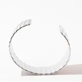 Brazalete rígido plateado con textura acanalada vertical.