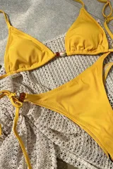 Conjunto de bikini amarillo con corpiño triangular con detalle de cuentas en el centro y bombacha semivedetina con tiritas ajustables y detalle de cuentas en los laterales.