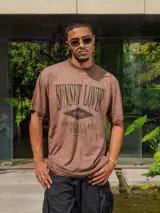 Remera de jersey con efecto teñido y corte holgado. Presenta una estampa frontal con el texto 'Sunset Lover' y 'You're my last sunburn' en color verde.