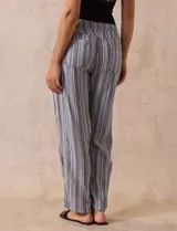 Pantalón largo de lino y rayón a rayas verticales grises y blancas. Tiene pretina elastizada con lazo de ajuste, bolsillos delanteros y traseros.