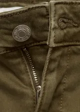 Pantalón de jean color verde oliva, de tiro medio, corte acampanado y largo al tobillo. Presenta bolsillos de parche delanteros y traseros, trabillas para cinturón y ruedo desflecado.