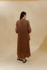 Vestido largo color beige, confeccionado en lino, con escote en V con volados y apliques de puntilla en las mangas. Posee bolsillos delanteros y tajos laterales.