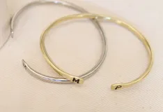 Pulsera rígida abierta en color dorado, con iniciales grabadas en los extremos.