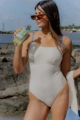 Traje de baño entero color blanco hueso, con textura gofrada o de punto en relieve. Presenta un escote recto y tirantes finos de color azul claro.