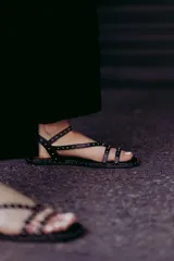 Sandalias chatitas negras de cuero con múltiples tiras finas y tachas doradas.