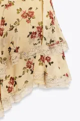 Minifalda color crema con estampado floral en tonos rojos y verdes. Presenta volados con puntilla en el ruedo.