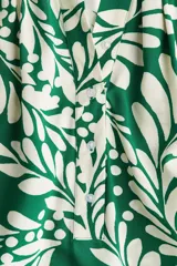 Blusa de tejido liviano color verde con estampado de hojas blancas, cuello corto fruncido y tapeta de botones. Mangas globo largas con volumen de corte raglán y puños finos abotonados.