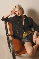 Camisa negra de tencel con bordados de canutillos, piedras, mostacillas y detalles en velvet a tono en el delantero y espalda. Tiene calce recto, manga larga, cuello camisero, puños con botón y cartera delantera con botones metálicos.