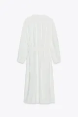 Vestido midi blanco de crepe con cuello redondo y escote pico, manga larga con puños y cinturón de la misma tela con hebilla metálica. Cierre frontal con botones metálicos.