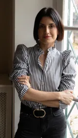 Camisa a rayas verticales blancas y negras, con cuello mao con volados, mangas largas abullonadas y cierre frontal con botones.