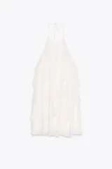 Minivestido blanco con cuello halter ajustable con lazos y falda escalonada con volantes. Espalda descubierta.