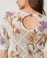 Top de tejido calado color crema con estampado floral en tonos lila, naranja y verde. Tiene cuello redondo y mangas cortas.