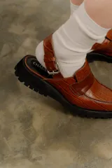 Zueco negro con textura croco, diseño tipo mocasín y tira regulable al talón.