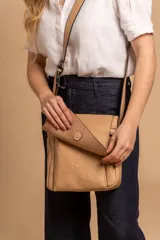 Bandolera de hombro color gris claro, con solapa frontal y correa ajustable. Presenta un diseño simple y práctico, ideal para uso diario.