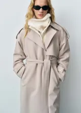 Trench color beige con solapas, trabillas en los hombros y puños, cinturón desmontable y bolsillos laterales.
