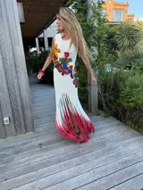 Vestido largo de tejido crochet blanco, sin mangas, con apliques bordados multicolores en el torso y flecos largos teñidos en degradé de blanco a fucsia en el ruedo.